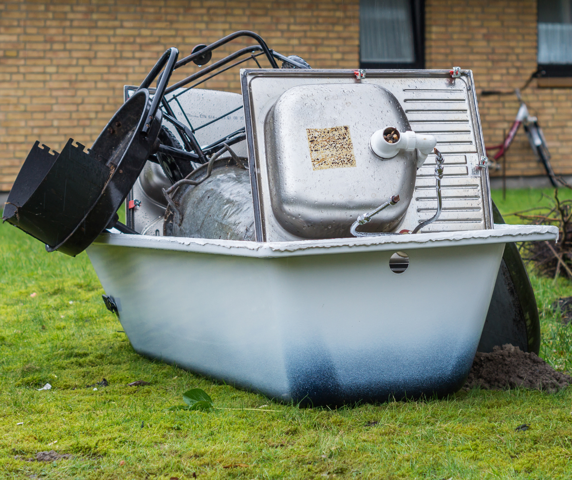 A pile of scrap metal, including an old bath and draining board, piled up on a lawn.